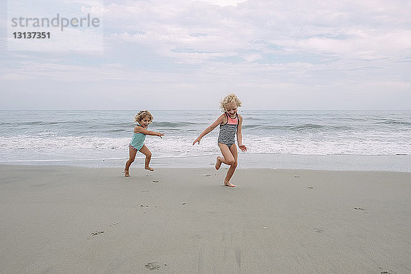Glückliche Schwestern spielen am Cape May Beach gegen Himmel und Meer