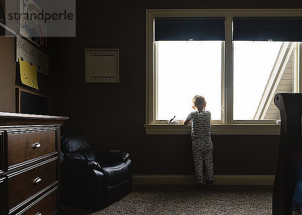 Rückansicht eines Jungen  der durch ein Fenster schaut