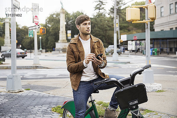 Mann mit Mobiltelefon auf dem Fahrrad in der Stadt sitzend