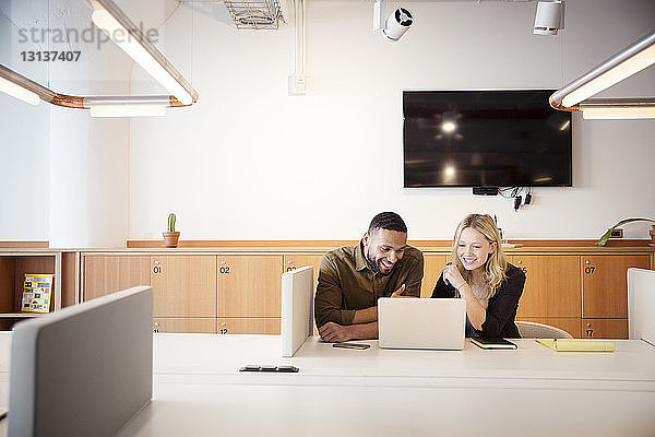 Kollegen benutzen Laptop-Computer  während sie im Büro am Tisch sitzen