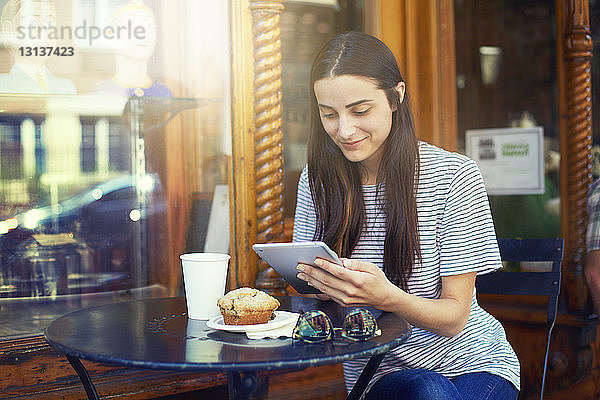 Lächelnde Frau benutzt digitales Tablet  während sie im Straßencafé an einem Tisch sitzt