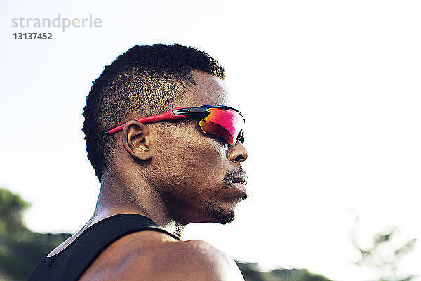 Niedrigwinkelansicht eines nachdenklichen männlichen Sportlers mit Sonnenbrille bei klarem Himmel
