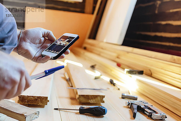 Beschnittenes Bild eines Tischlers  der in der Werkstatt fotografiert