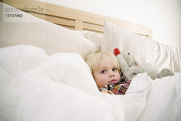 Porträt eines süßen Jungen mit Plüschtier  der sich zu Hause auf dem Bett ausruht