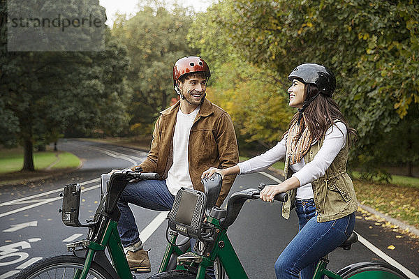 Lächelndes Paar unterhält sich im Stehen mit Fahrrädern auf der Straße im Park
