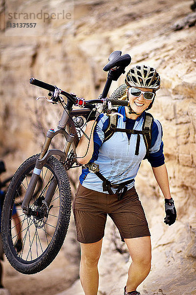 Porträt einer Frau  die beim Wandern auf dem Berg ein Fahrrad trägt
