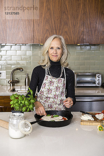 Porträt einer selbstbewussten älteren Frau  die zu Hause in der Küche Pizza zubereitet