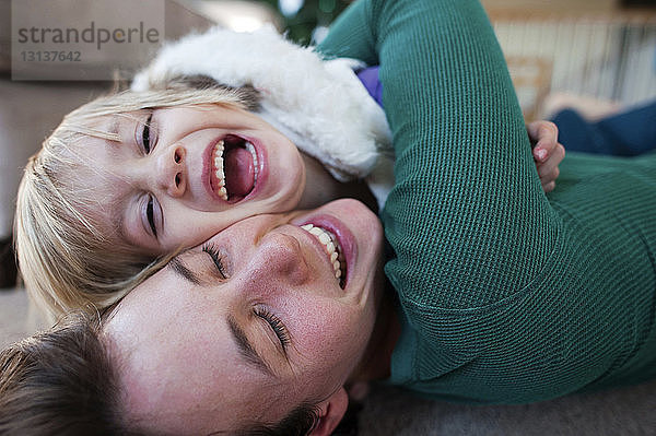 Glückliche Mutter umarmt Tochter  während sie zu Hause auf dem Teppich liegt