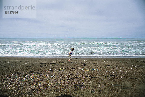 Mädchen rennt auf Sand am Strand gegen bewölkten Himmel