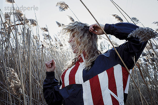 Fröhliche Frau trägt Jacke mit amerikanischer Flagge beim Tanzen inmitten von Pflanzen auf dem Feld