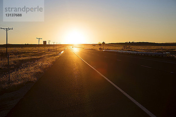 Straße mitten im Feld gegen klaren Himmel bei Sonnenuntergang