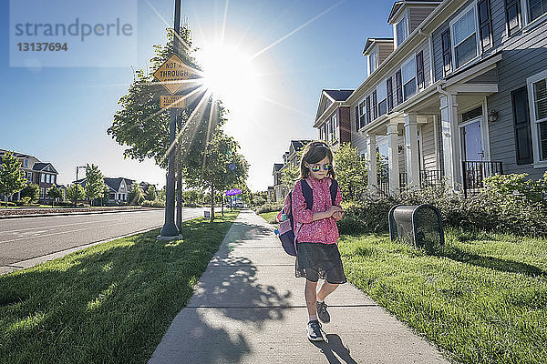 Mädchen mit Rucksack  das eine Sonnenbrille trägt  während es auf einem Fußweg gegen den klaren Himmel am sonnigen Tag läuft