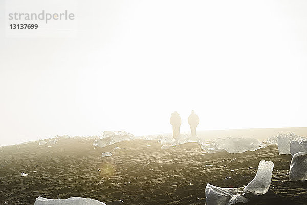 Silhouetten von Menschen mit Eisformationen am Ufer vor klarem Himmel bei Sonnenschein