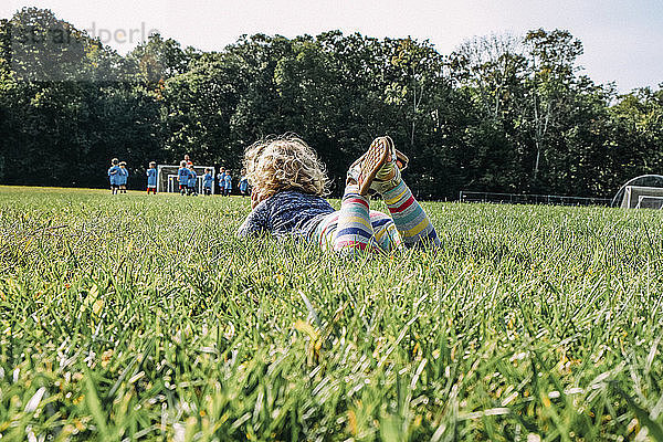 Mädchen sieht sich ein Fußballspiel an  während sie auf dem Rasen eines Spielplatzes liegt