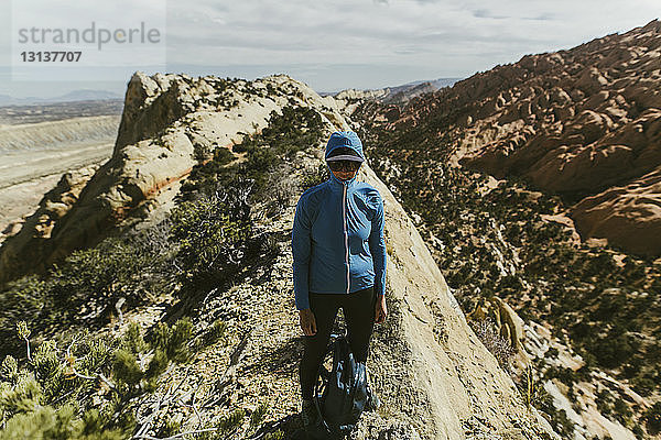 Wanderin mit Rucksack  die Jacke und Mütze trägt  während sie am sonnigen Tag am Berg steht
