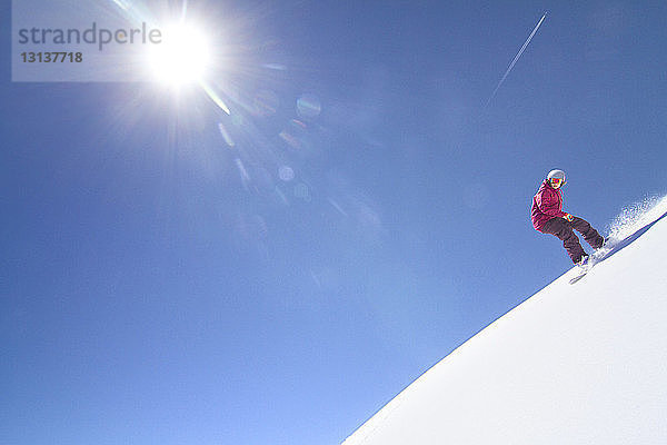 Niedrigwinkelansicht einer Snowboarderin beim Abstieg vom Schneefeld gegen klaren Himmel