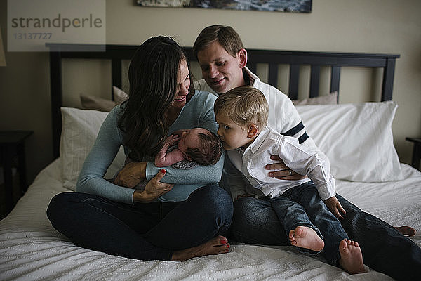 Familie mit neugeborenem Jungen zu Hause im Bett sitzend