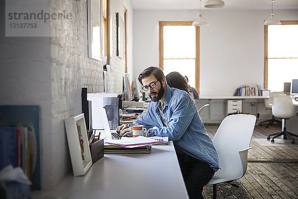 Geschäftsmann benutzt Laptop  während er im Kreativbüro sitzt