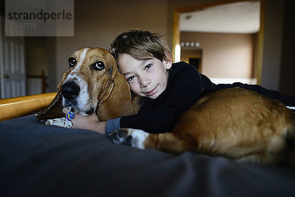 Porträt eines Jungen  der einen Hund umarmt  während er auf dem Bett liegt