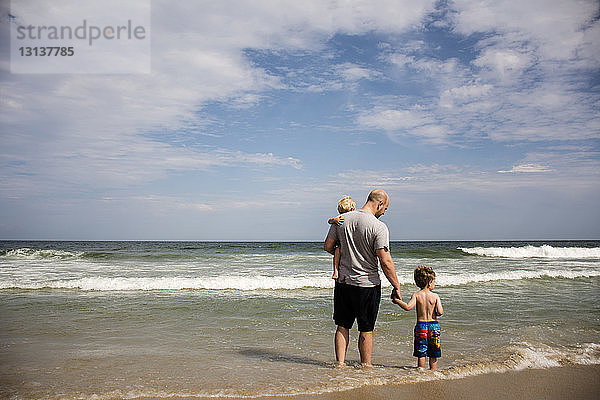 Rückansicht einer Familie  die an einem sonnigen Tag am Strand gegen den Himmel genießt