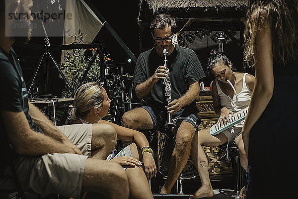 Mann und Frau spielen Musikinstrumente  während sie mit Freunden am Ferienort sitzen