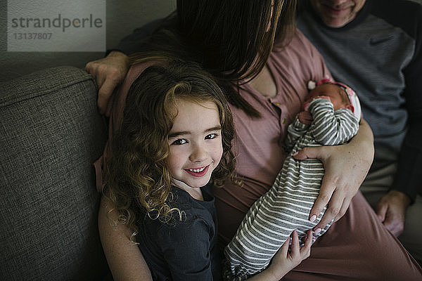 Hochwinkelporträt eines lächelnden Mädchens mit Eltern und Schwester auf dem Sofa zu Hause