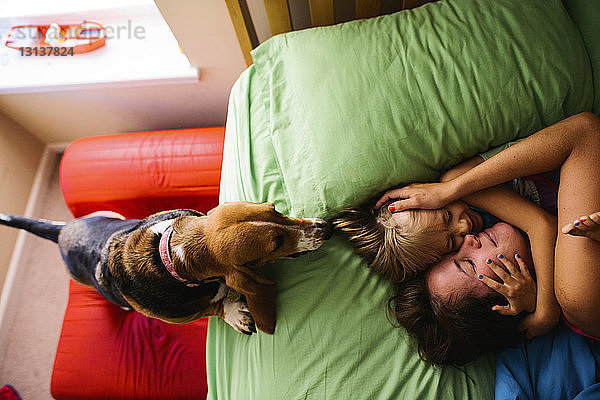Draufsicht eines Hundes  der Mutter und Tochter sieht  wie sie sich zu Hause im Bett umarmen