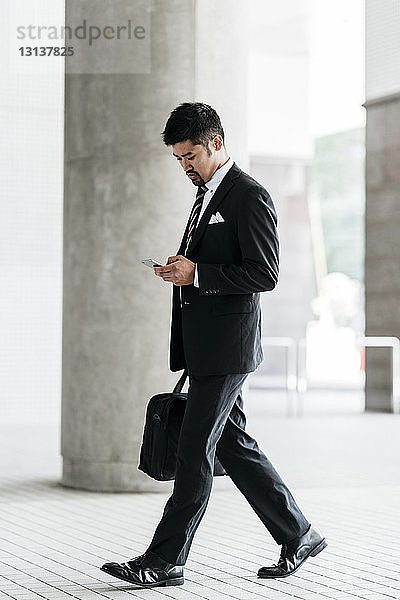 Geschäftsmann in voller Länge mit Smartphone beim Gehen an der Kolonnade