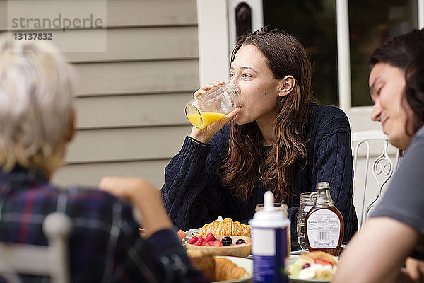 Frau schaut weg  während sie mit Freunden am Frühstückstisch Orangensaft trinkt