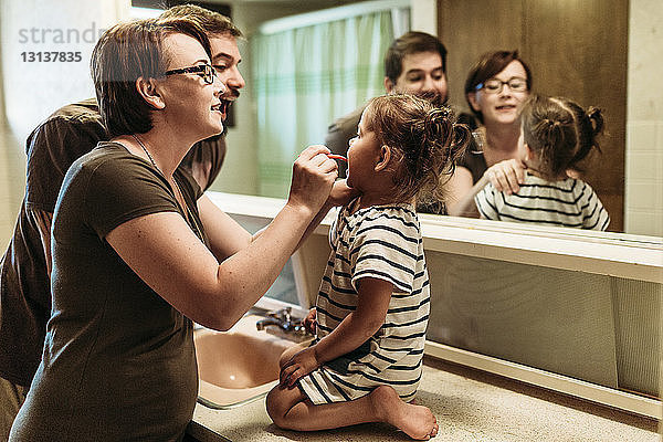 Vater steht bei der Mutter und putzt der Tochter im Badezimmer die Zähne