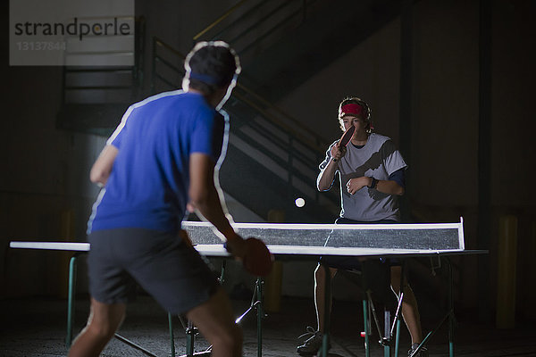 Männer spielen Tischtennis gegen beleuchtetes Gebäude