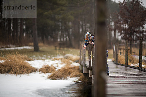 Mitteldistanzansicht eines Jungen  der im Winter im Park auf einem Holzsteg über den Fluss spielt