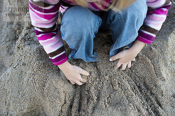 Hochwinkelaufnahme eines Mädchens  das am Strand mit Sand spielt