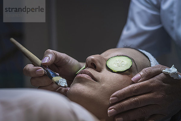 Geschorene Hände einer Kosmetikerin beim Auftragen einer Gesichtsmaske auf eine Kundin im Ästhetischen Zentrum