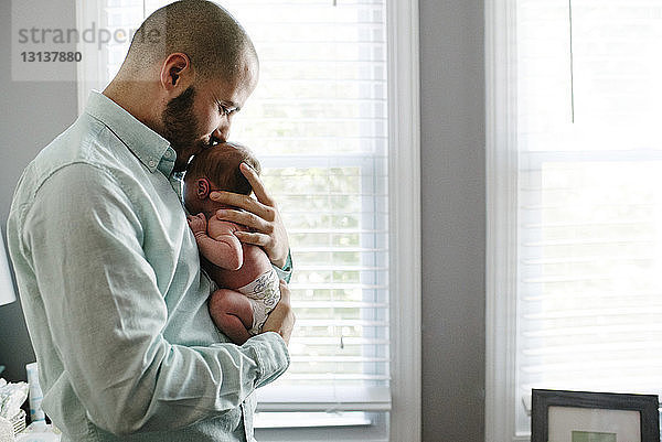Seitenansicht eines Vaters  der seine neugeborene Tochter küsst  während er sie zu Hause trägt