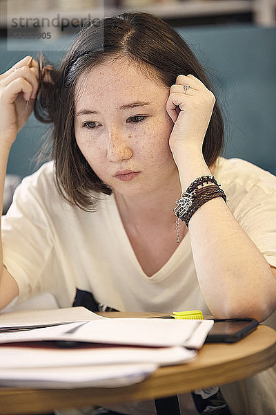 Nahaufnahme einer nachdenklichen jungen Frau mit Büchern  die zu Hause wegschaut