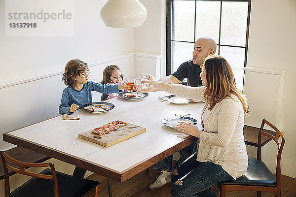 Familien erheben einen feierlichen Toast  während sie zu Hause am Esstisch sitzen