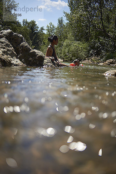 Mutter und Tochter schwimmen bei Sonnenschein im Fluss im Wald