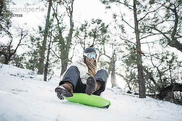 Glückliche Frau fährt auf Schlitten in schneebedecktem Feld