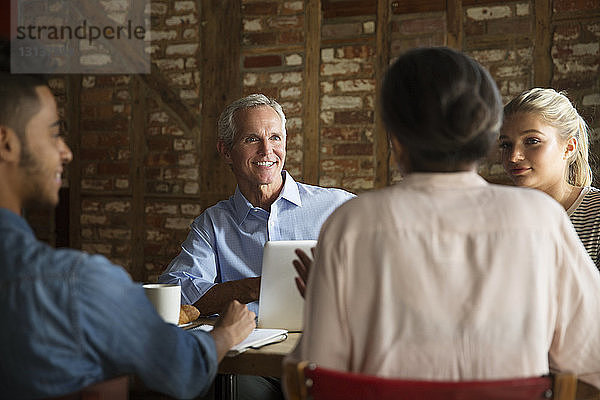 Lächelnder Geschäftsmann hört Kollegen während eines Treffens im Café zu