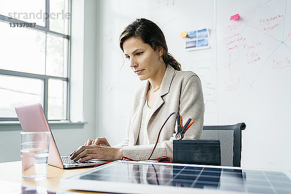 Geschäftsfrau benutzt Laptop-Computer  während sie im Büro an einem Whiteboard sitzt