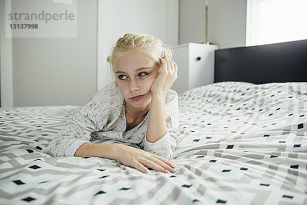 Gelangweiltes Mädchen schaut weg  während es zu Hause auf dem Bett liegt