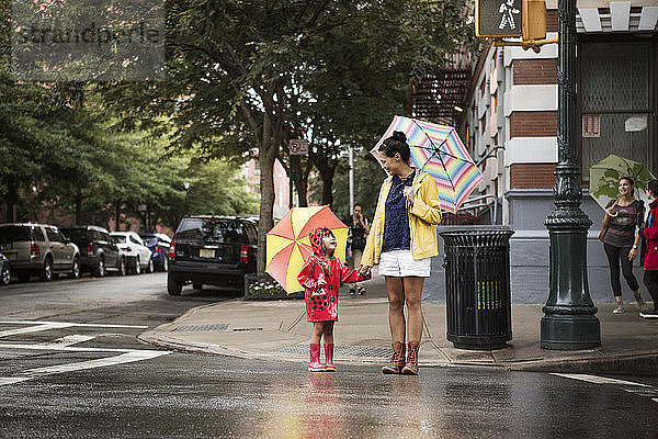 Mutter und Tochter schauen sich an  während sie auf der Straße Regenschirme halten