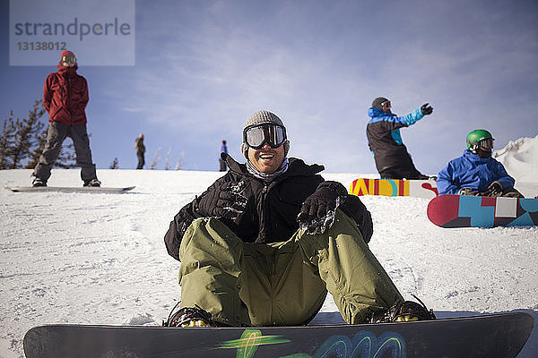Fröhliche Freunde beim Snowboarden auf verschneitem Feld gegen den Himmel