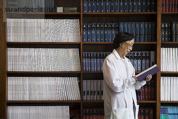 Seitenansicht einer leitenden Wissenschaftlerin beim Lesen eines Buches an den Regalen im Labor