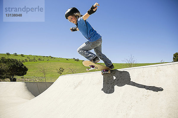 Niedrigwinkel-Ansicht eines Skateboard fahrenden Jungen auf der Rampe vor klarem blauen Himmel