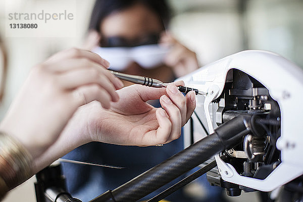 Ausgeschnittenes Bild einer Studentin  die an einer Drohne arbeitet  mit einem Freund im Hintergrund