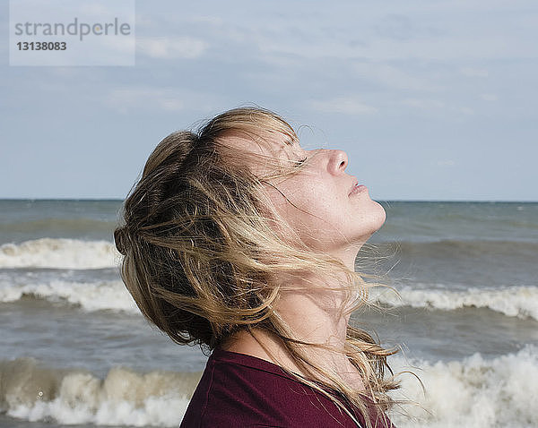 Seitenansicht einer Frau mit geschlossenen Augen  die während eines sonnigen Tages am Meer gegen den Himmel steht