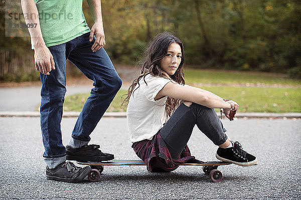 Frau sitzt auf Skateboard mit Mann auf der Strasse