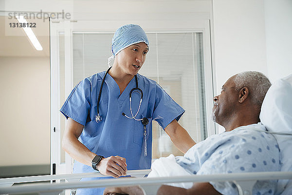 Seriöser Chirurg im Gespräch mit älterem Patienten  der auf der Krankenhausstation im Bett liegt